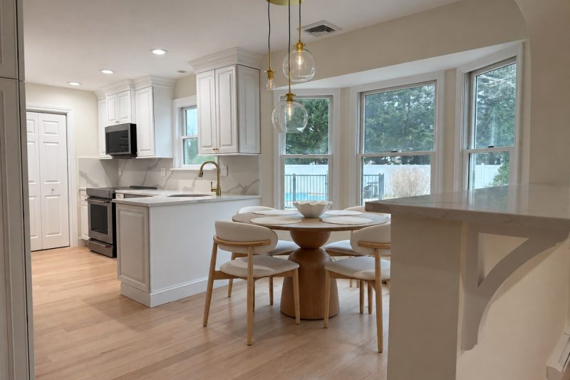 Dix Hills kitchen and breakfast area with white cabinets, veined countertops and a round wood dining table.